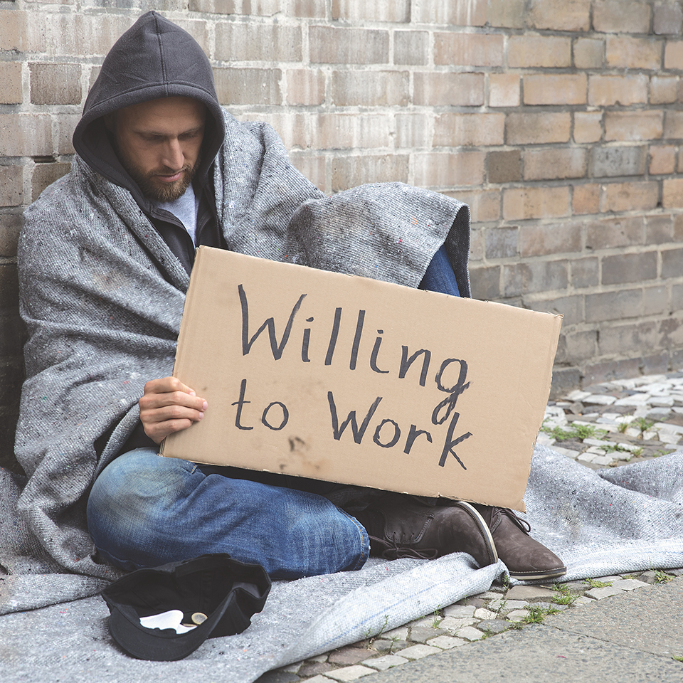 Homeless Man In Hood Sitting On Street Holding Cardboard With Text Willing To Work